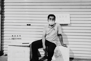 一个戴着口罩的年轻人坐在车库前的长椅上的黑白照片