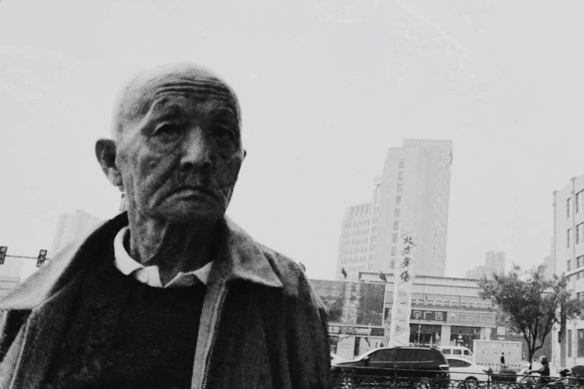 这是一张黑白照片 内容是一位老人在街上步行。