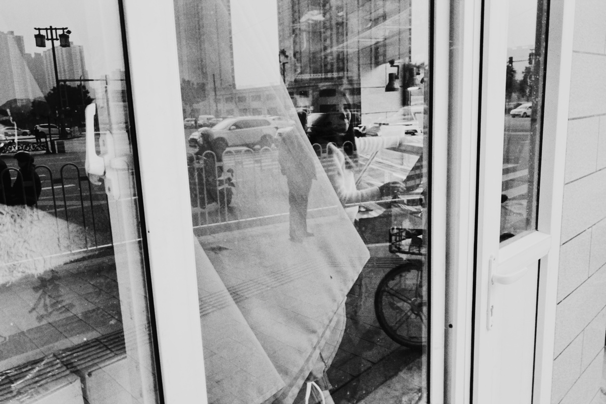 这是一张黑白的照片 一个男子正对着商店的窗户看 外面有一辆自行车挂在窗外。