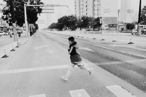 这是一个穿着黑白衣服的小男孩或女孩在空荡荡的街道上奔跑。