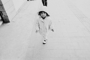 一个穿着雨衣的小女孩在人行道上奔跑 一个年轻男孩沿着街道步行。