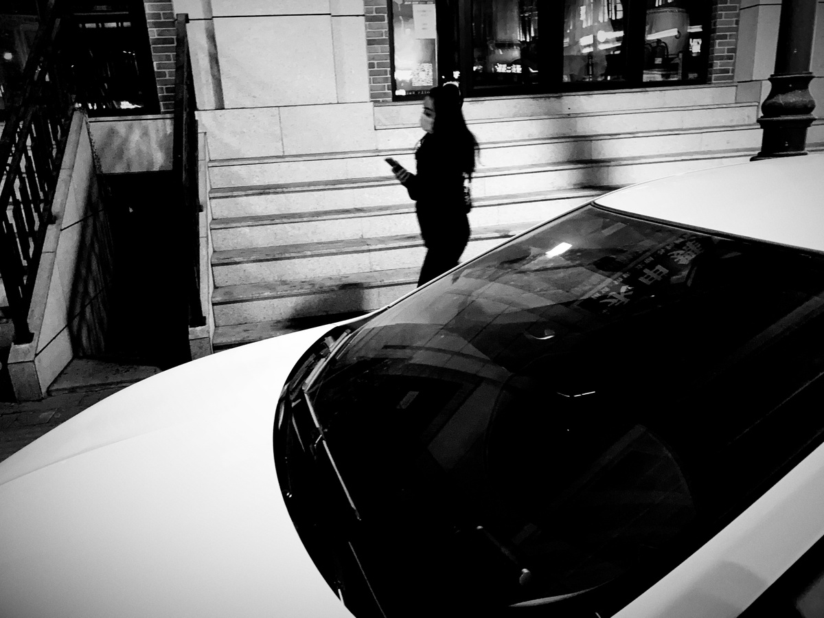 夜晚停在街道上的黑白汽车 一名男子站在车顶使用手机。