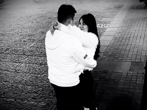 一张黑白照片 一个男子拥抱着一个年轻的女人站在人行道上。