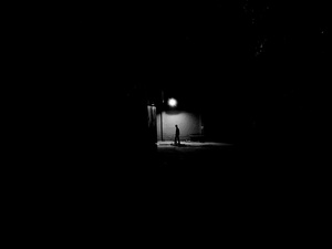 夜晚的黑暗街道上 一个人站在一盏灯下。