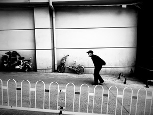 一个黑白照片 展示一个人沿着围栏走下街道 旁边停着自行车。