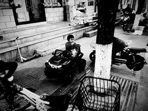 一个黑白照片 一个男子坐在摩托车上 旁边停着一辆停在街上的汽车。