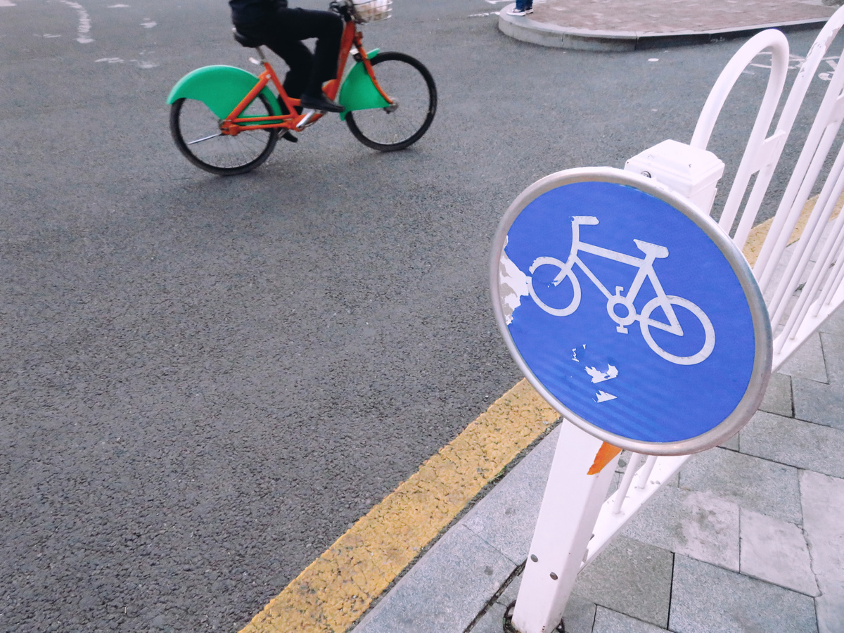 一个人骑着绿色的自行车沿着蓝色的白色标志牌下的街道