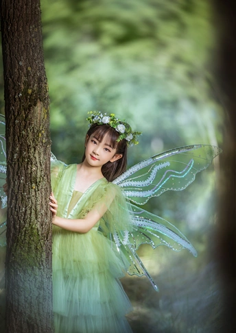 在美丽的绿色森林里 一个打扮成仙女的小女孩靠在树上