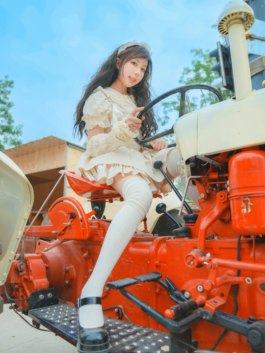 一个穿着白色衣服的女孩在旧拖拉机上摆姿势 带有方向盘