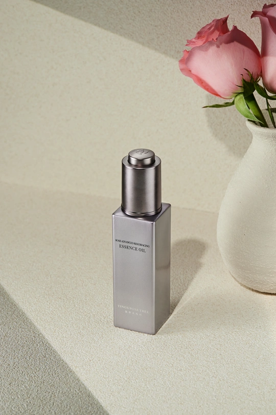 一瓶香水 放在柜台旁边 旁边有一个插着粉色玫瑰花的白色花瓶。