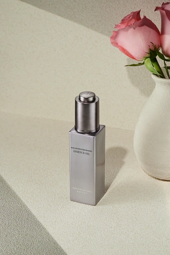 一瓶香水 放在柜台旁边 旁边有一个插着粉色玫瑰花的白色花瓶。