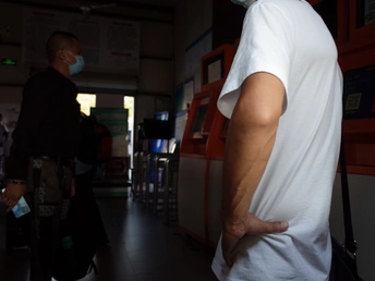 一名身穿白衬衫、戴着口罩的男子走在走廊上 背景是其他人