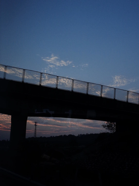 黄昏或日落时在水面上飞越天桥的飞机