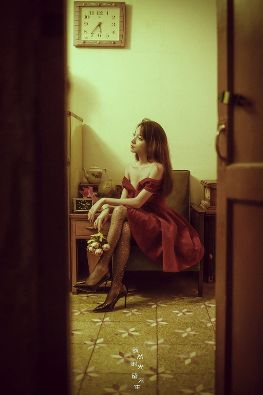 一个穿着红裙子的年轻女子坐在一个有钟的房间里的一把椅子上