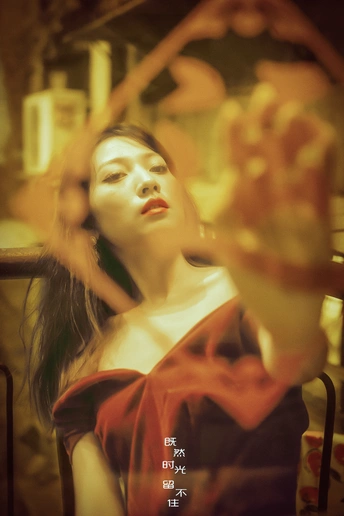 一位穿红裙子的女人站在镜子后面 桌子上有一朵花。