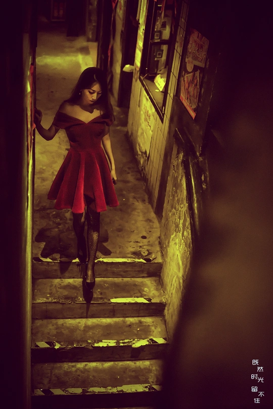 一个穿着红色连衣裙的年轻女子打着伞走在一个黑暗的巷子里