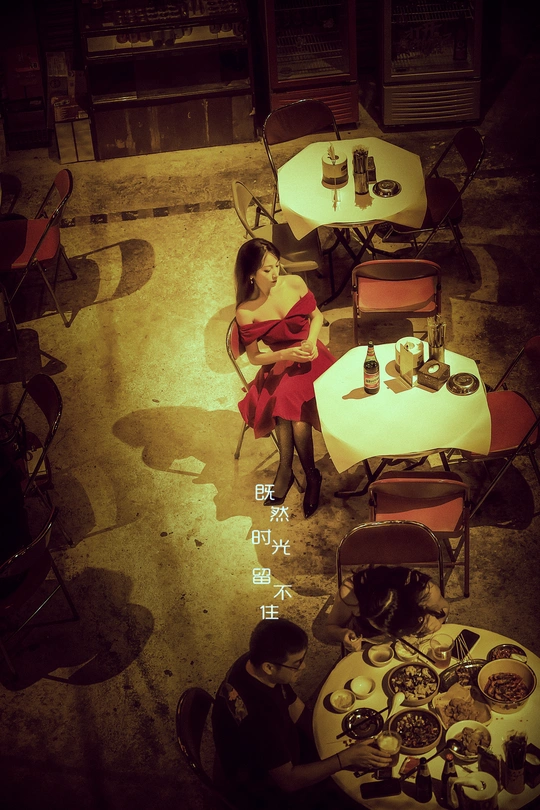 一位穿着红裙子的女人坐在餐厅的一张桌子旁 桌子上放着盘子 里面装着食物。