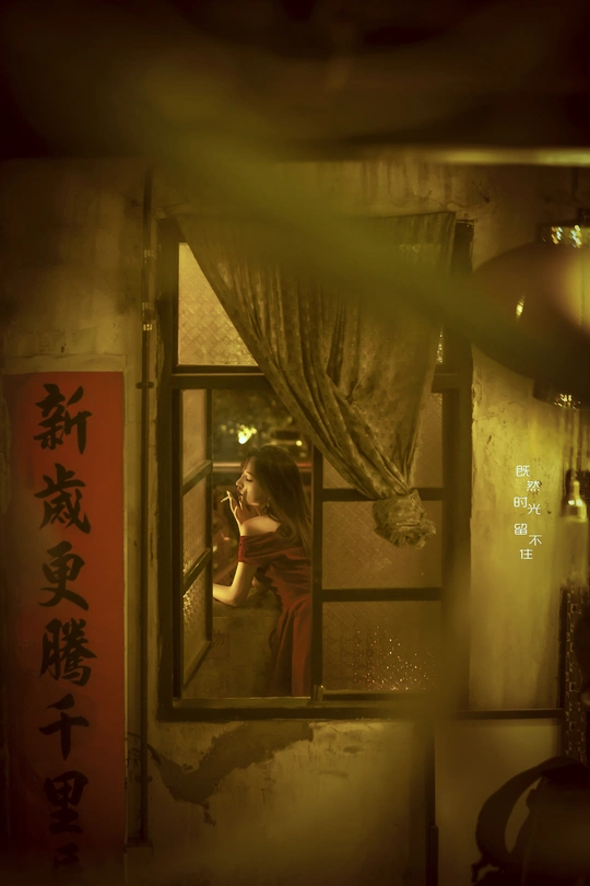 一位站在窗户前的女人正在用镜子里的房间里的自己的倒影拍照。