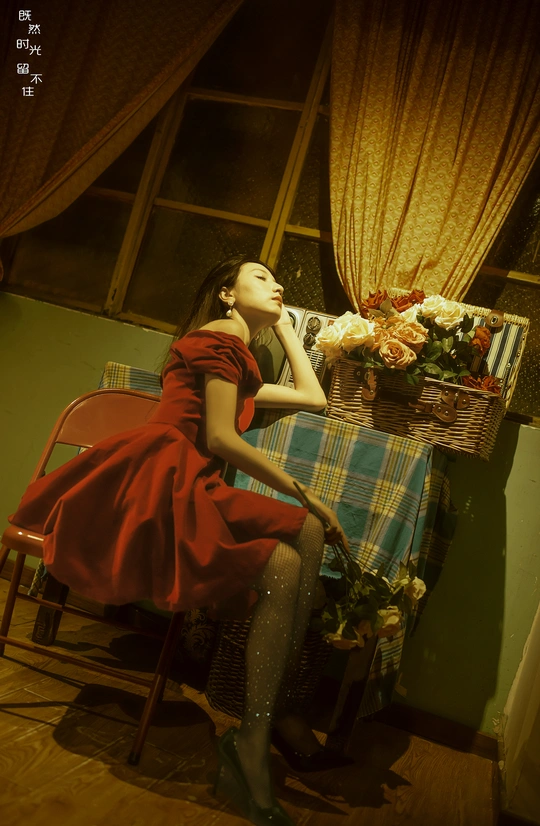 一个穿着红裙子的年轻女子坐在一个装满花的篮子旁的椅子上。
