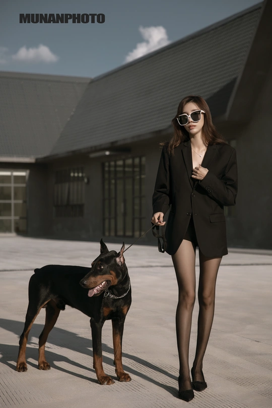 一个戴太阳镜的美女站在一只黑狗旁边