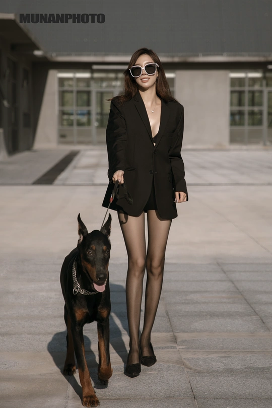 一个穿黑色西装的女人正在遛一只黑色狗。