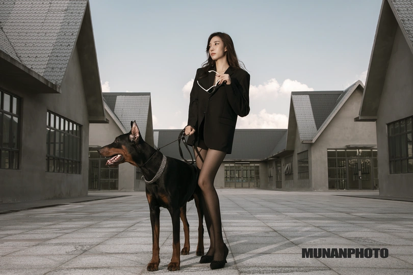 一个美丽的年轻女子站在一只黑棕色的狗旁边