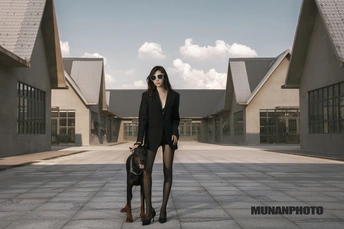 一个穿着黑色高跟鞋的年轻女子在空荡的庭院中与她的狗合影。