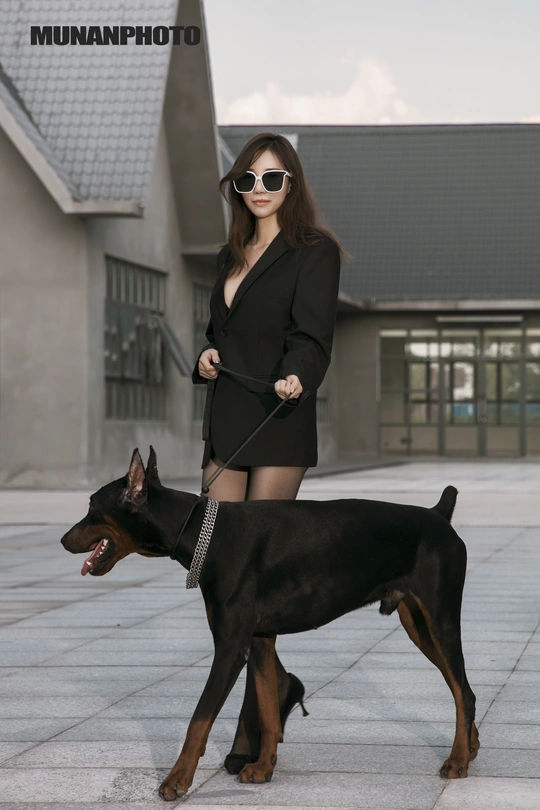 一个年轻女子站在遛狗绳上牵着一只黑狗