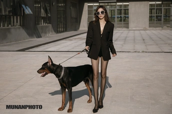 一位年轻女子站在一只黑棕色的狗旁边