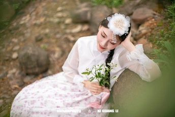 一位穿着传统服装的年轻女子抱着花坐在岩石上森林中