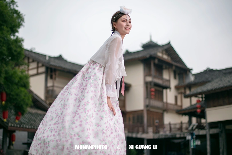 一位穿着传统服装的年轻女子在老建筑前持伞站立。