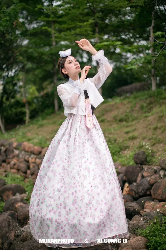 一个穿着粉红色和白色连衣裙的女孩在森林中的岩石上