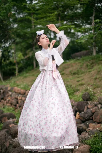 一个穿着粉红色和白色连衣裙的女孩在森林中的岩石上