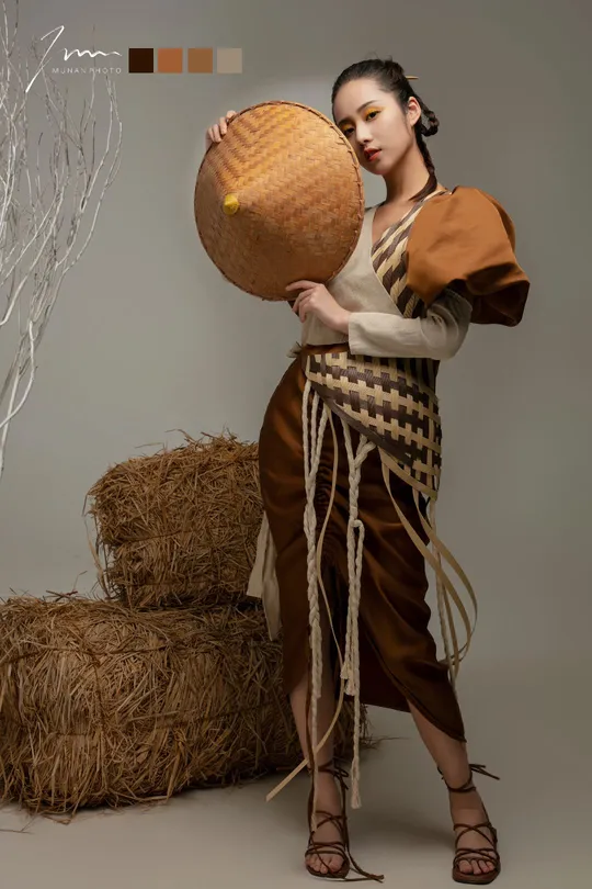 一位穿着costume的年轻女子手持一顶帽子站在一捆干草前面