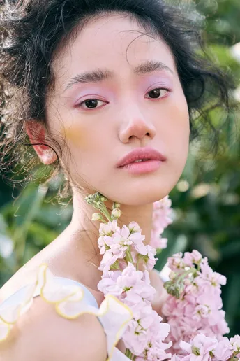 一位美丽的年轻女子卷发 为肖像摆姿势 手中拿着粉色花朵。