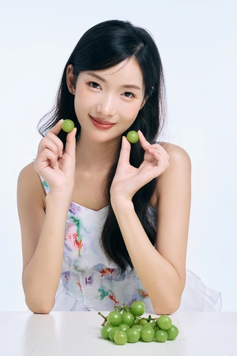 一位年轻女子手里拿着青翠欲滴的葡萄 用手指托着脸部姿势拍照。