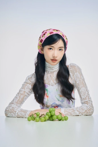 一个年轻女子坐在桌子上 头上有葡萄 还有绿苹果。