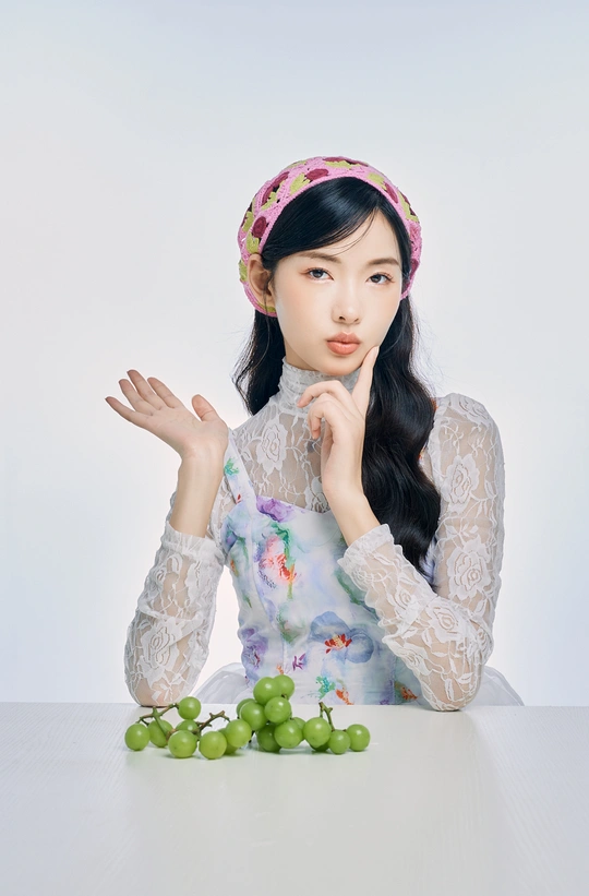 一个年轻女子坐在白色桌子旁 头上有绿葡萄 双手捂住脸