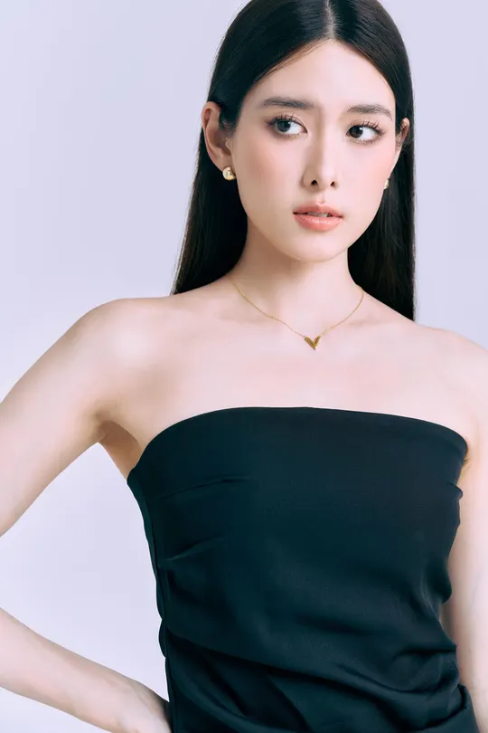 一位穿着黑色连衣裙和项链的女性在白色背景前摆姿势