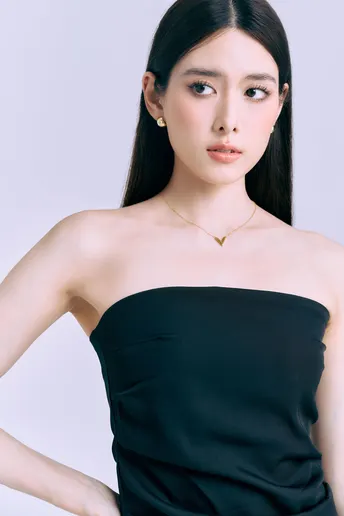 一位穿着黑色连衣裙和项链的女性在白色背景前摆姿势