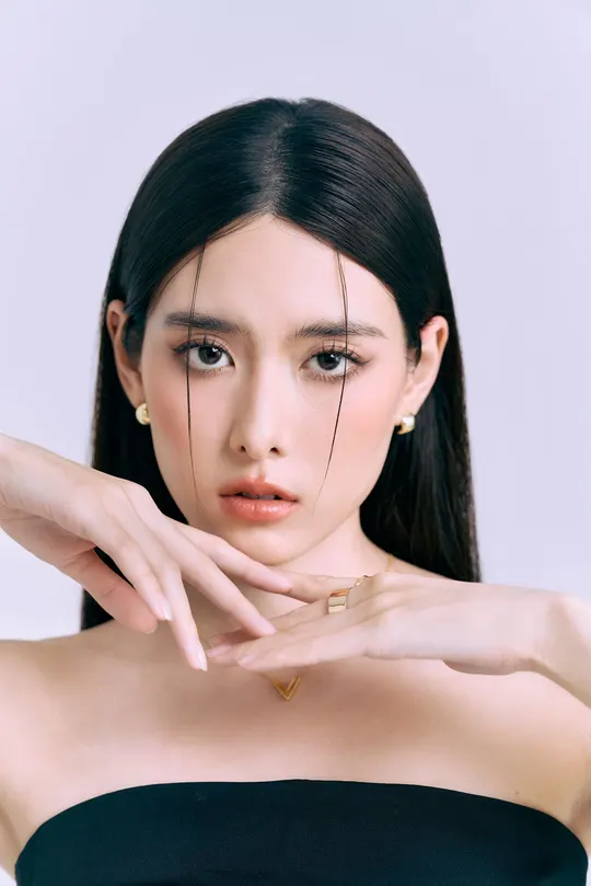 一位年轻女子穿着黑色连衣裙 双手捂住脸部 摆出姿势。