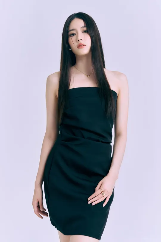 一位穿着黑色连衣裙的年轻女子在白色背景前摆姿势