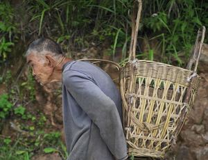沿着河的一名老年男子 carrying a basket