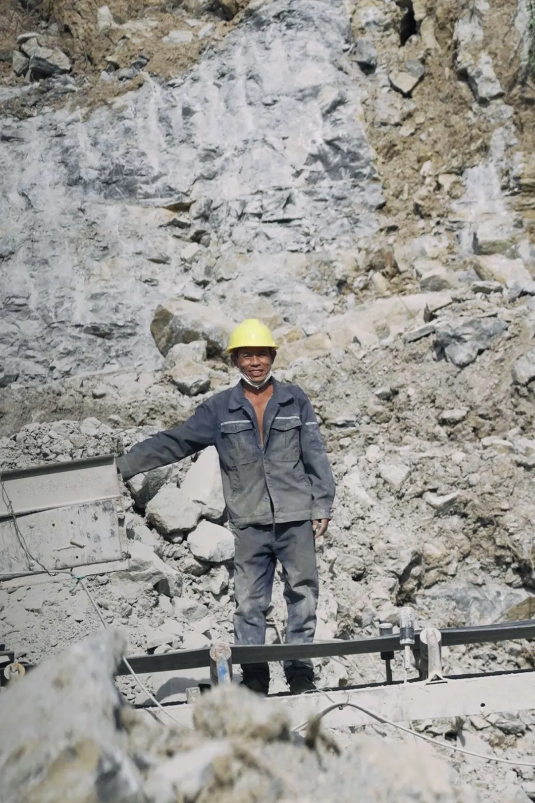 一个戴黄 hard hat 的人走过一座桥 背景中有岩石。