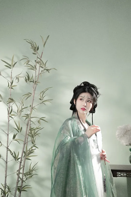 一尊穿着绿色连衣裙的女性雕像 手持雨伞 站在一棵绿色植物旁边。