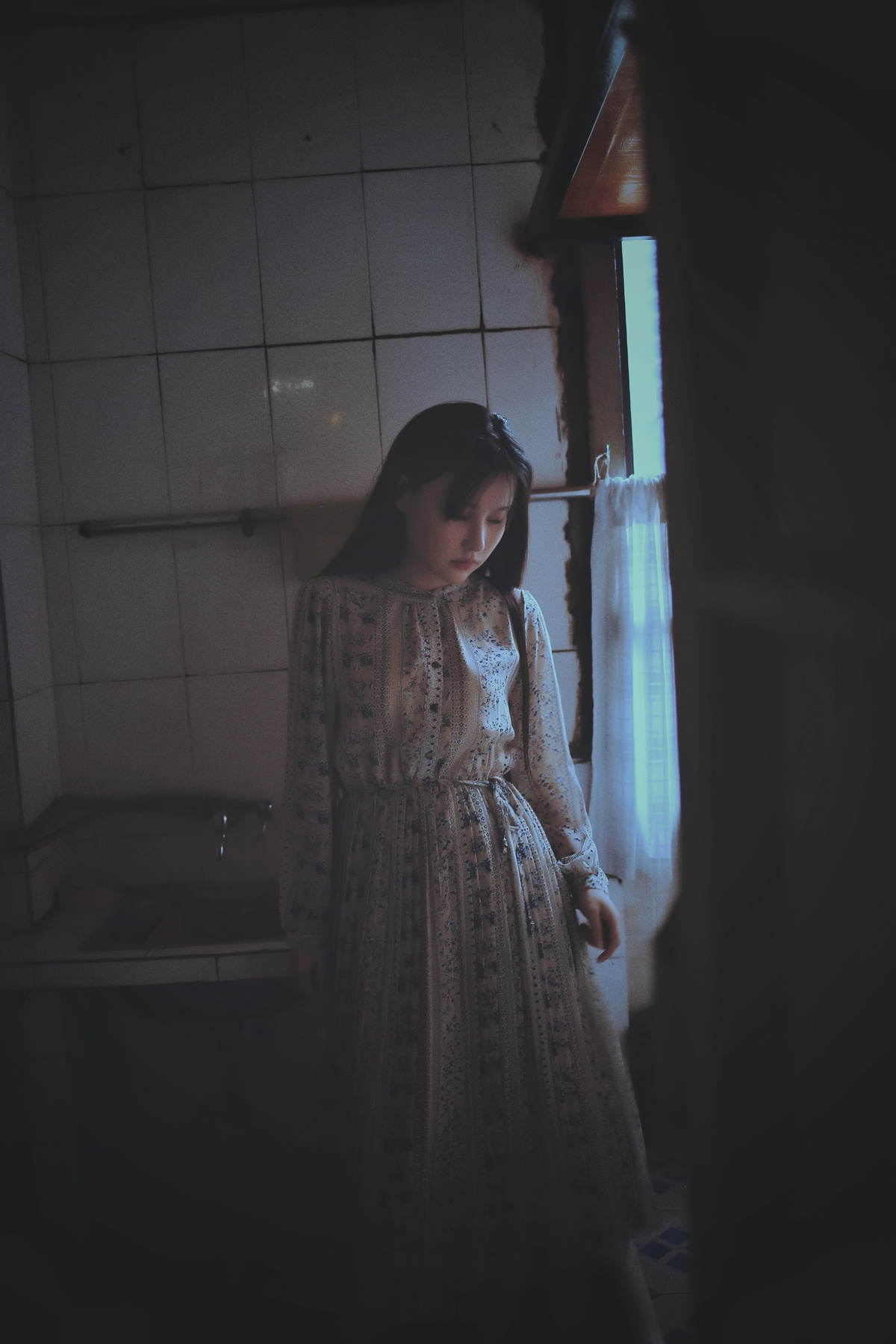 一个穿着白色连衣裙的年轻女子站在一个黑暗的房间里望着窗外