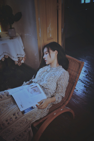 一个年轻的女人坐在一个房间的椅子上读杂志 手里拿着一本打开的书