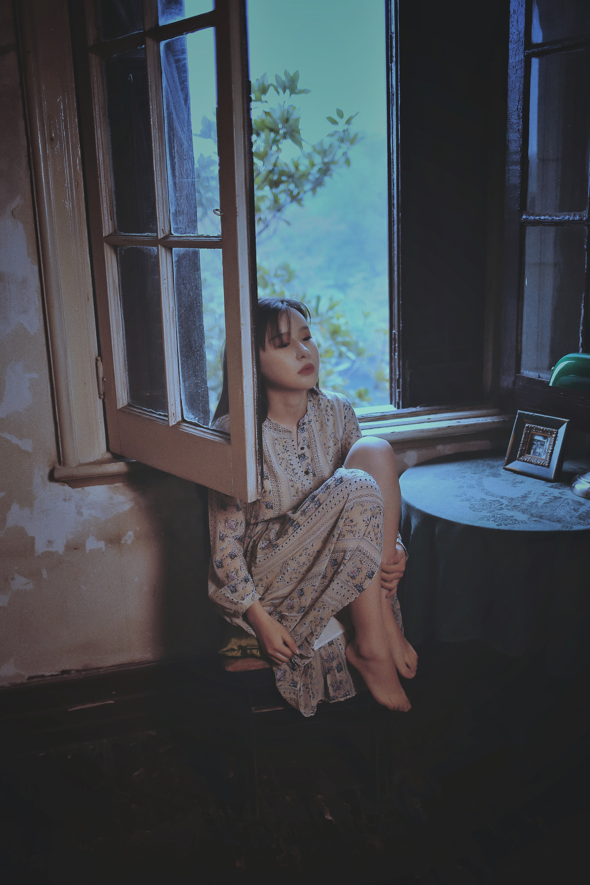 一个年轻的女人坐在开着的窗户旁 望着外面一个脏乱的房间
