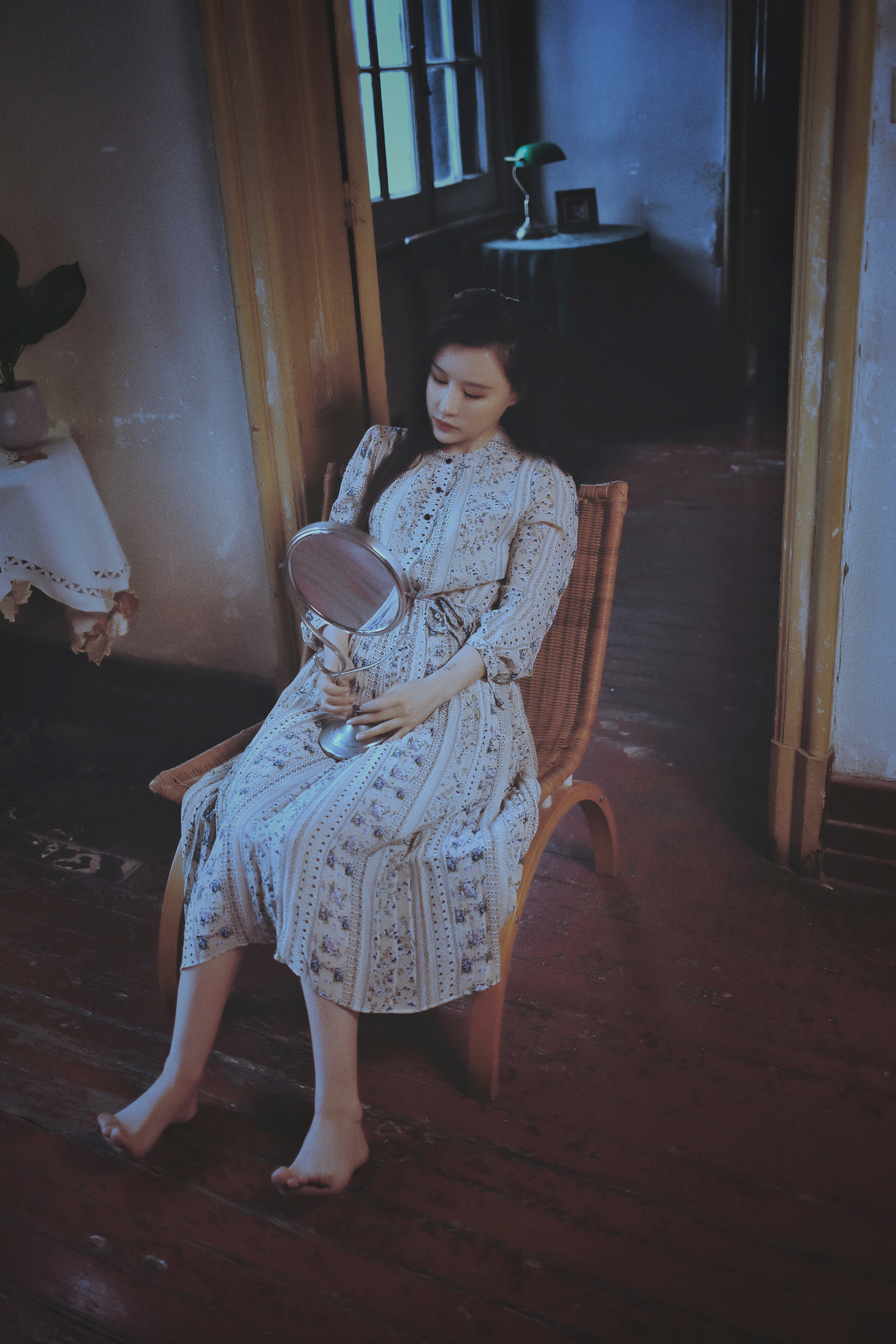 一个穿着连衣裙的年轻女人坐在一所老房子的椅子上看着镜子