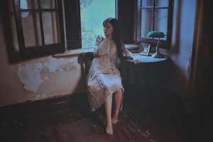一个穿着连衣裙的年轻女子坐在有窗户的房间里的椅子上